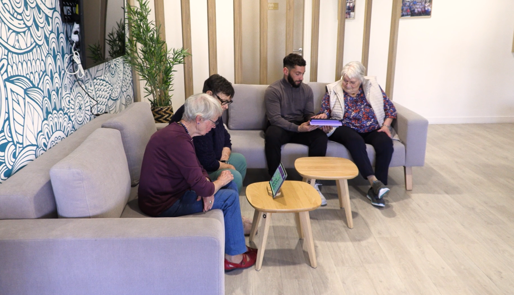 1 animateur de résidence senior joue avec 1 résidente sur une tablette à Gena-App. 2 résidentes senior jouent ensemble