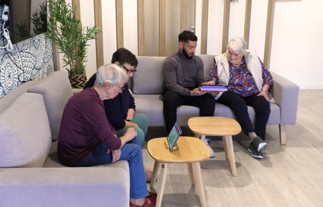 1 animateur de résidence senior joue avec 1 résidente sur une tablette à Gena-App. 2 résidentes senior jouent ensemble